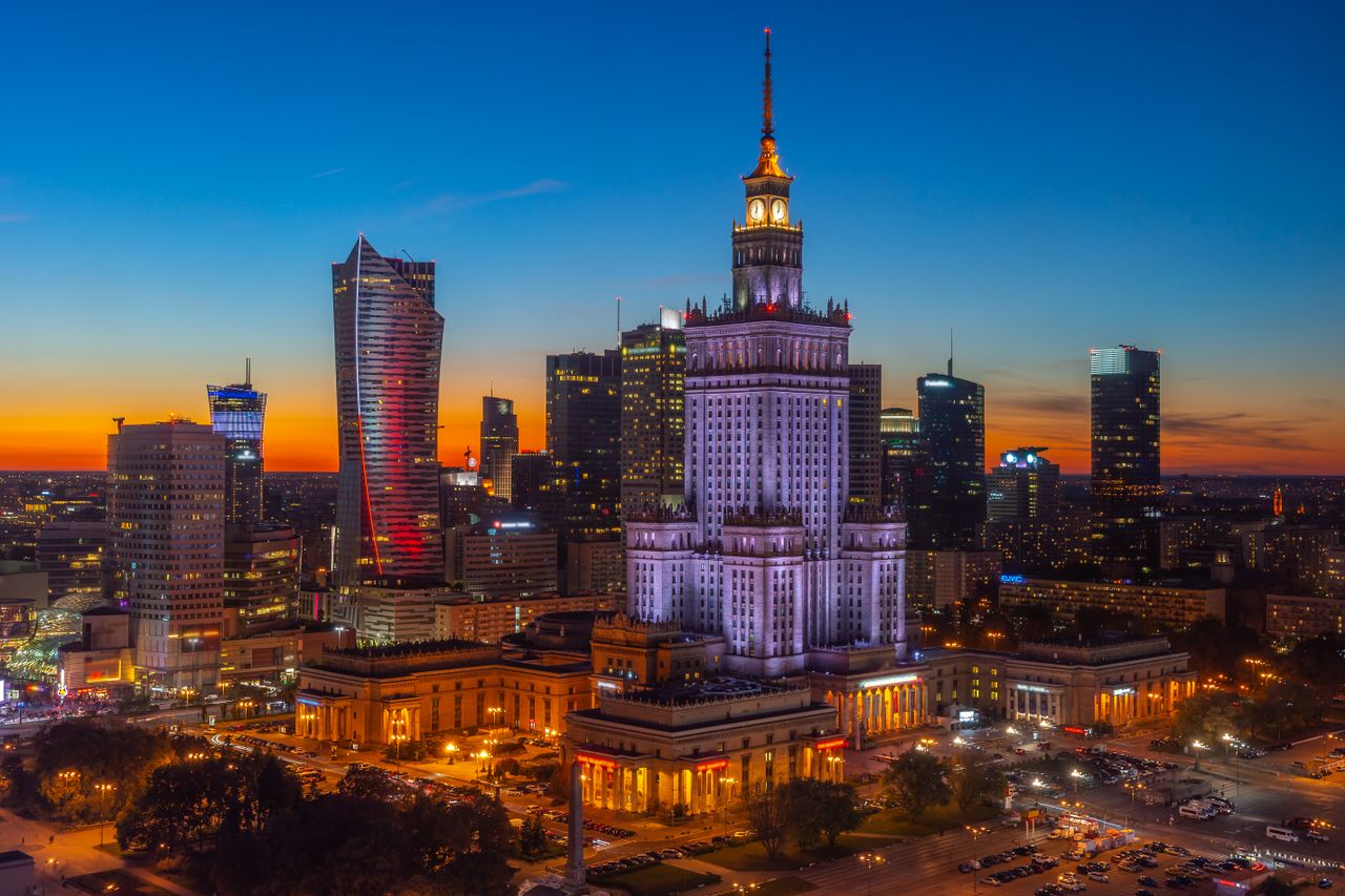 Aerial view of Warsaw's skyline at twilight, featuring the illuminated Palace of Culture and Science.