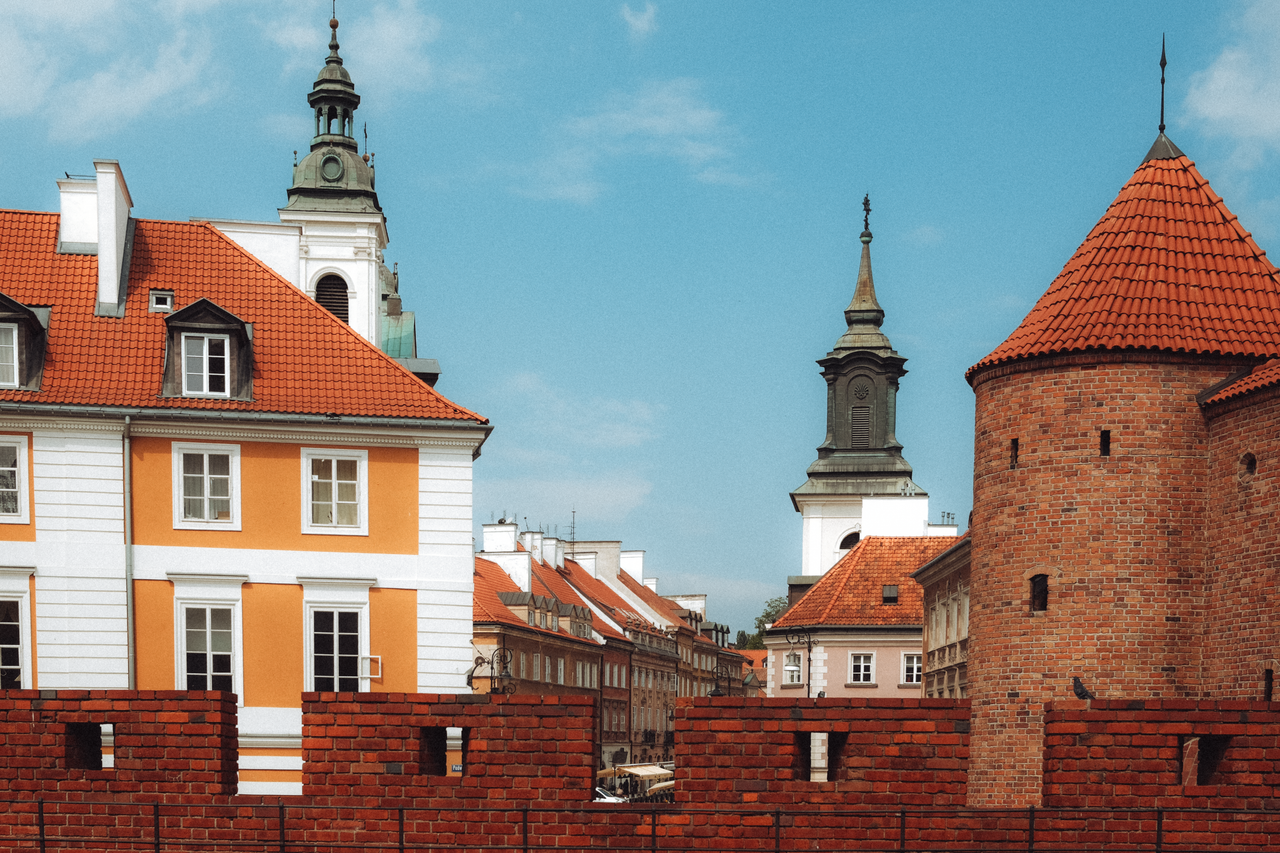 Charming view of historic buildings and brick tower in Warsaw's Old Town on a sunny day.