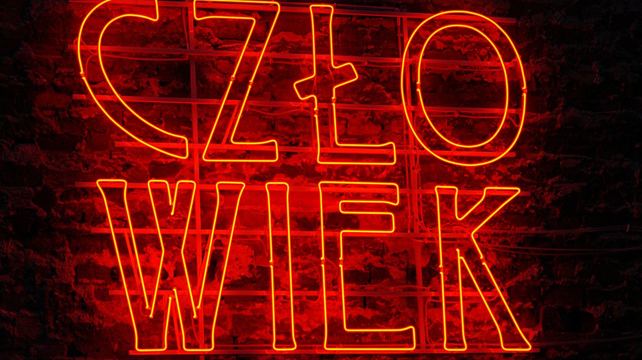 contact-img Glowing red neon sign reading 'CZŁOWIEK' on a dark brick wall, striking and bold.